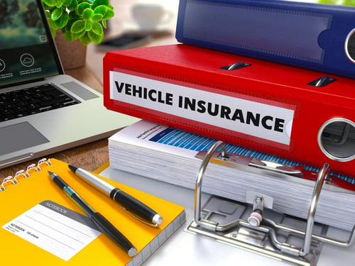 Red Ring Binder with Inscription Vehicle Insurance on Background of Working Table with Office Supplies, Laptop, Reports. Toned Illustration. Business Concept on Blurred Background.